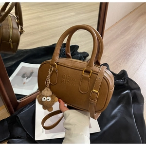 Détail du sac Boston en cuir marron foncé avec logo en relief et breloque en peluche