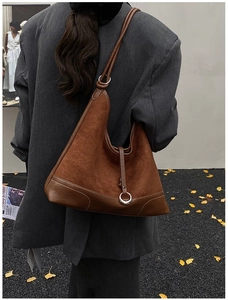 Detail van een bruine suède patchwork tas met metalen ring en gladde lederen riemen