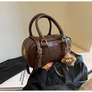 Détail du sac Boston en cuir marron foncé avec logo embossé et breloque en peluche