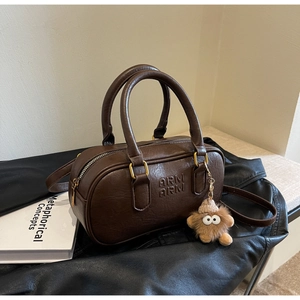 Détail du sac Boston marron foncé avec logo embossé et charm monstre en peluche
