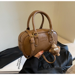 Détail du sac Boston en cuir marron avec grain de litchi, bijoux dorés et porte-clés