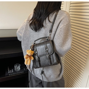 Détail du sac à dos en suédine grise avec boucles de ceinture et breloque ours en peluche
