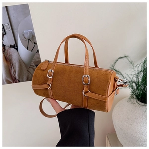 Detail of a brown cylindrical shoulder bag featuring suede texture and silver buckles