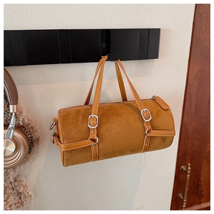 Close-up of brown suede cylinder bag with silver metal buckles and leather strap details