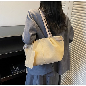 Detail of a beige suede tote bag with pleated design and a small matching pouch pendant