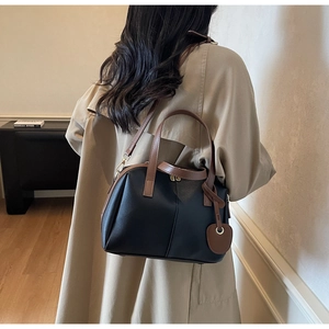 Femme portant un sac coquillage noir et marron avec breloque cœur sur un trench-coat