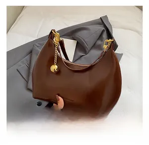 Dettaglio borsa hobo in pelle marrone scuro con catena dorata e ciondoli su blazer grigio