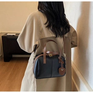 Vue détaillée du sac Boston rétro en cuir noir avec des lanières brunes et des breloques