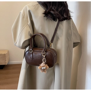 Détail d'un sac Boston marron avec gaufrage ARM ARM et breloque peluche sur un trench-coat