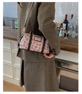 Close-up of pink leopard print cylinder bag with leather handles and brand label