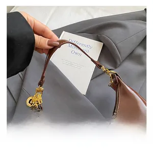 Dettaglio borsa hobo in pelle lucida marrone con catena dorata e ciondolo in metallo