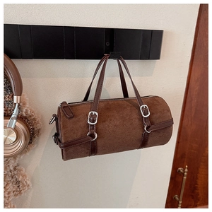 Detail of a dark brown suede cylinder bag hanging on a rack with glossy leather straps