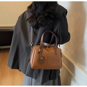 Sac Boston marron en similicuir avec détails dorés et breloque cœur porté par le mannequin