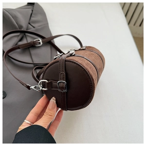 Close-up of brown cylinder shoulder bag with silver buckle and suede texture details