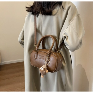 Détail du sac polochon rétro marron avec texte embossé et charmant monstre en peluche