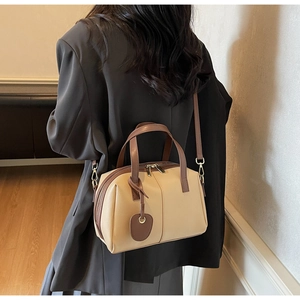 Détail d'un sac à main beige et marron porté avec blazer noir et jupe plissée