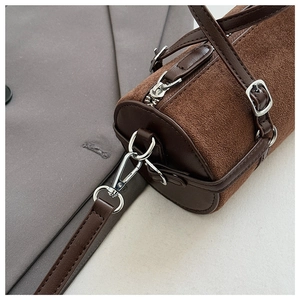 Detail of brown suede cylinder bag with silver metal zipper and smooth leather accents
