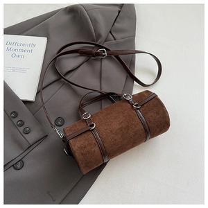 Detail of dark brown cylindrical handbag with suede texture on a grey suit background