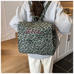 Detail of green leopard canvas backpack featuring red script embroidery and metal buckle