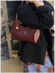 Dettaglio della borsa hobo bordeaux lucida con ciondolo a sfera dorata sulla modella