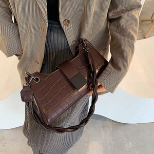 Detail of dark brown crocodile pattern handbag with twisted strap and metallic buckle