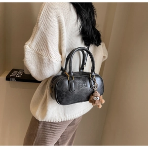 Détail du sac Boston vintage noir avec logo embossé et pendentif en peluche marron
