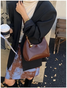 Dettaglio borsa hobo in pelle marrone scuro con ciondolo dorato in un ambiente urbano