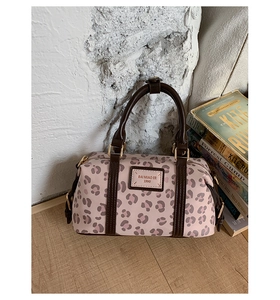 Detail of pink leopard print Boston bag with leather handles and gold-tone hardware on wood