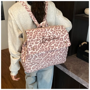 Detail of pink leopard print canvas backpack showing embroidery and flap closure on model