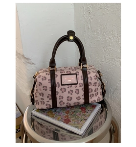 Close-up of pink leopard print boston bag with leather logo tag and brown handles