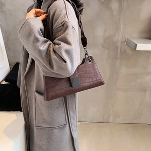 Dark brown faux crocodile underarm bag with twisted handle shown on model's shoulder