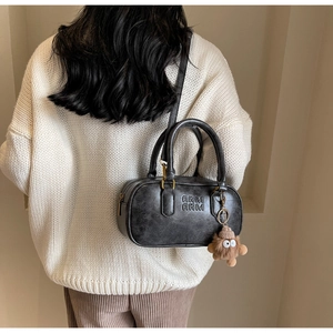 Détail du sac polochon rétro gris foncé avec lettres embossées et breloque en peluche