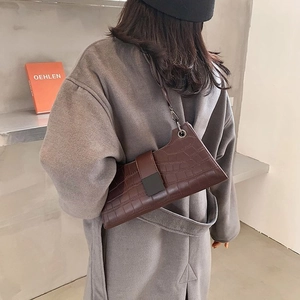 Detail of dark brown crocodile-embossed leather bag with geometric cut and square buckle