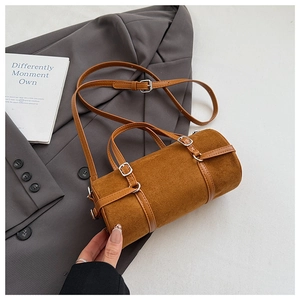 Detailed shot of brown cylinder bag with suede texture and metal buckle on grey blazer