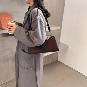 Detail of dark brown crocodile embossed leather shoulder bag styled with a grey coat