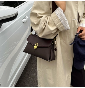 Detail of a dark brown vintage crossbody bag with a gold oval twist lock on a beige trench coat