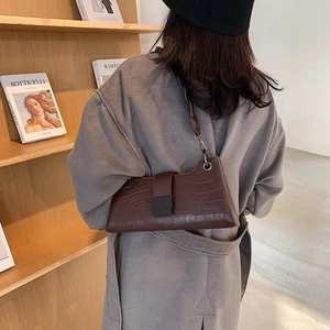Model wearing dark brown crocodile pattern shoulder bag against a bookstore backdrop