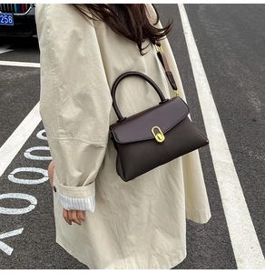 Detail of dark brown retro crossbody bag featuring a golden oval lock and wide strap