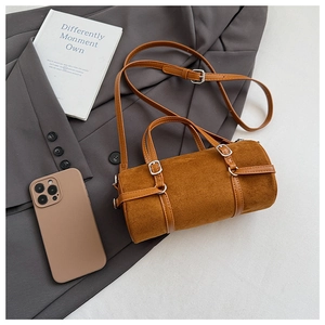 Detail of a brown cylindrical bag with suede texture and adjustable leather shoulder strap