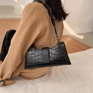 Detail of black crocodile texture shoulder bag with twisted strap on a model