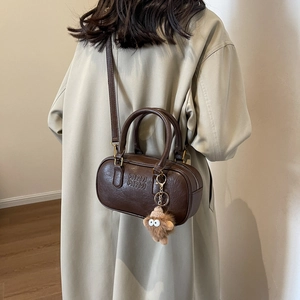 Sac Boston vintage marron avec breloque en peluche sur fond de mannequin en manteau