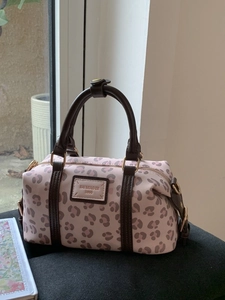 Pink leopard print Boston bag with brown handles and gold hardware on a textured stool