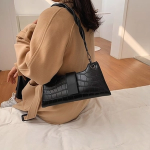 Detail of black crocodile pattern shoulder bag with a unique woven twisted strap design