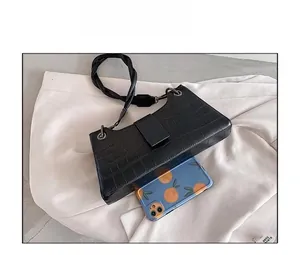 Detail of crocodile pattern shoulder bag next to phone for size comparison