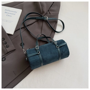 Close-up of teal suede cylinder bag with leather straps on a brown blazer background