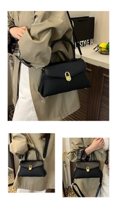Close-up of black leather handbag with gold oval twist lock and adjustable shoulder strap