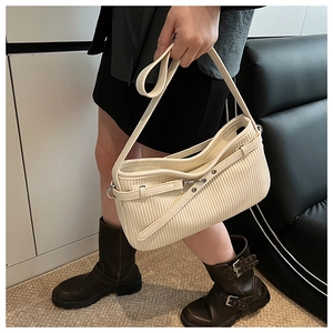 Détail d'un sac en cuir souple crème présentant des plis verticaux et une boucle en métal