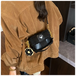 Detail of black woven crossbody bag with gold chain strap and donut charm on shoulder