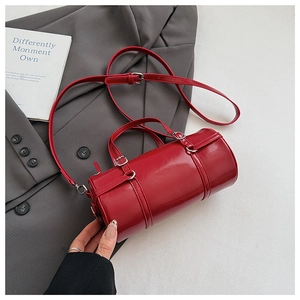Detail of red cylindrical Boston bag with glossy finish and silver hardware on grey fabric