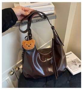 Detail of a dark brown glossy hobo bag with a cute plush bear pendant and wide strap